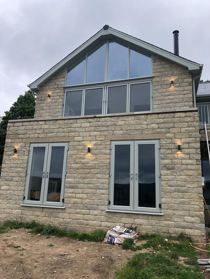 Stone double-storey extension with full-height gable glazing and French doors